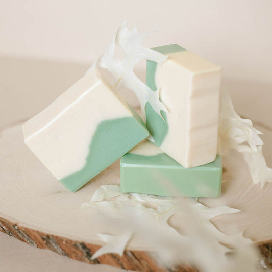 Three bars of handmade soap with green and white mountain design on a wooden surface.