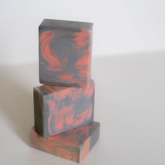 Three stacked rectangular bars of soap with a marbled pattern of dark gray and burnt orange, set against a plain light gray background.