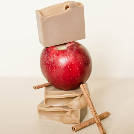 Red apple with a beige bar of soap on top and cinnamon sticks on a beige background