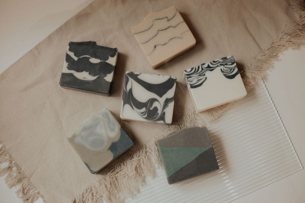 Six handmade, artisanal soaps arranged in a circular formation. Designs varying with waves, swirls and landscapes.