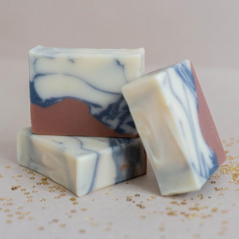 Three handmade all-natural bars of soap colored with cream and indigo powder swirls over a mountainous layer of peach French clay. Scented with an essential oil blend of litsea, cedarwood atlas and ylang ylang.