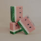 Three handmade bars of soap stacked in angles. Watermelon layers of pink, white, green and speckled with black tear-drop seeds. Scented with watermelon sugar fragrance oil from Brambleberry.