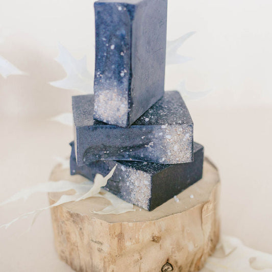 Three black handmade bars of soap, sprinkled with white  bath salts.