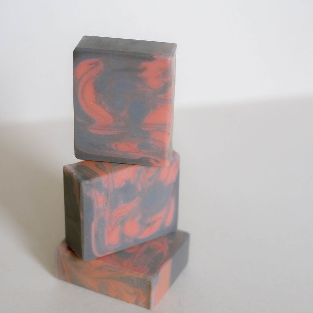 Three stacked rectangular bars of soap with a marbled pattern of dark gray and burnt orange, set against a plain light gray background.