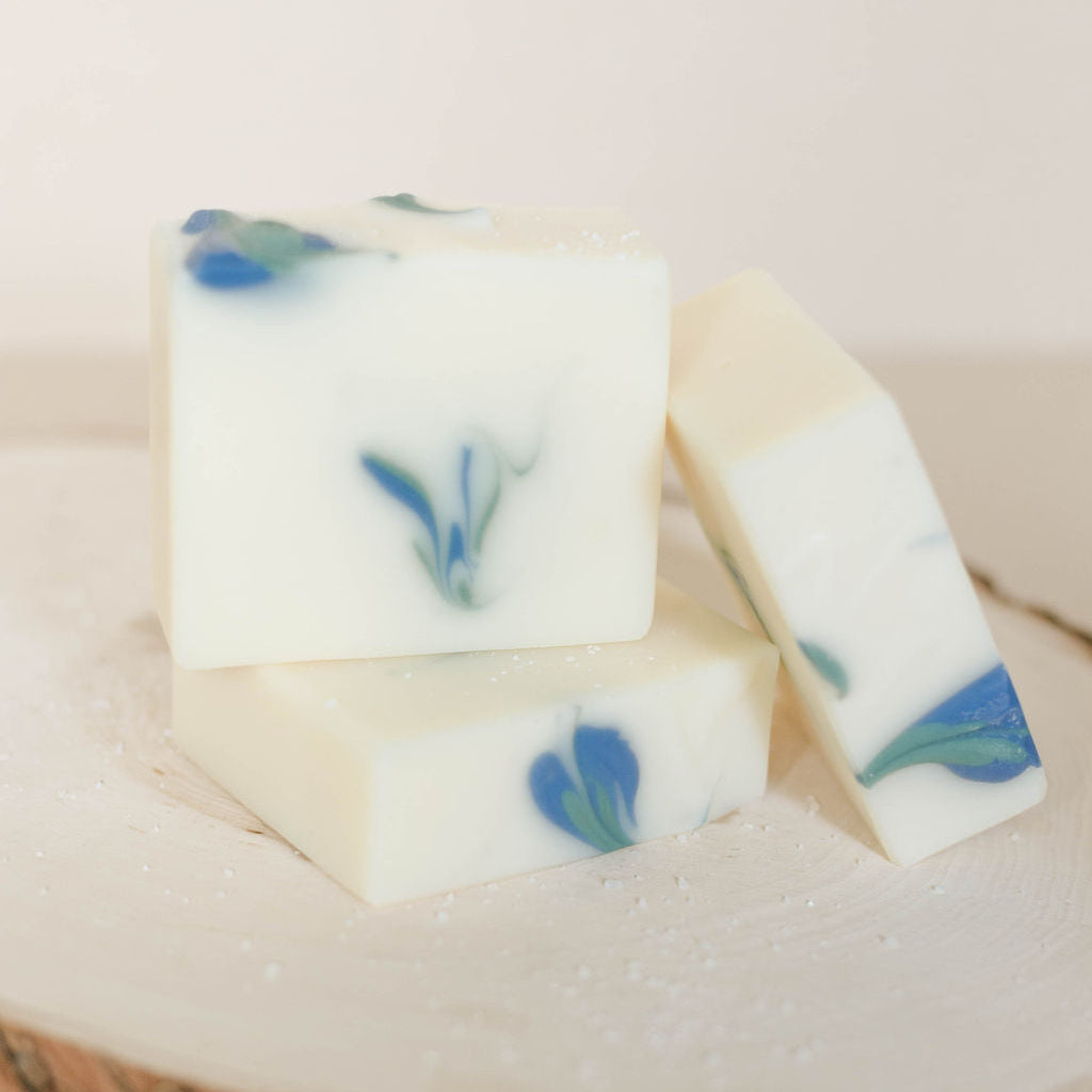 Three creamy white bars of handmade soap accented with blue and green flower swirls in the center. Scented with Brambleberry's Sea Salt and Lily fragrance oil.