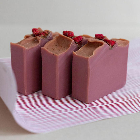 Three handmade bars of soap colored in a pink mauve with accents of dried pomegranate flowers on top. Scented with Bramble Berry's Santa's Spruce fragrance oil.