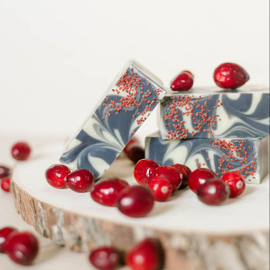 Three handmade bars of soap swirled with activated charcoal propped on hardwood with cranberry accents.