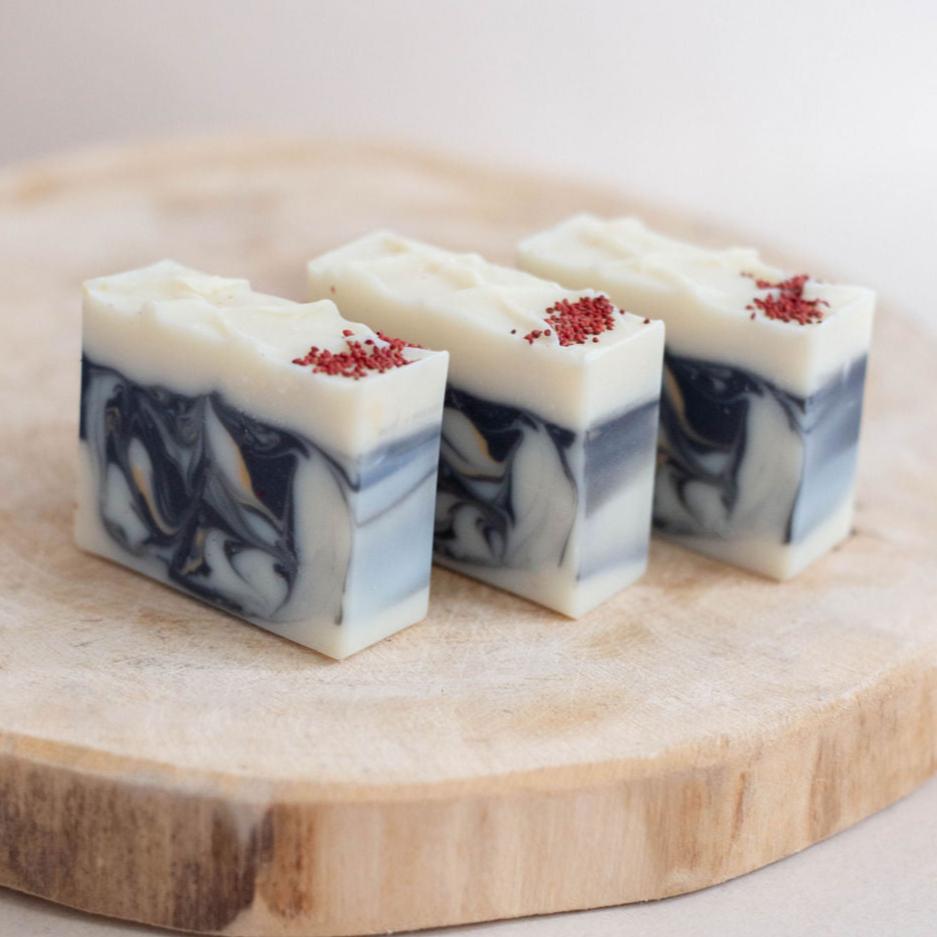 Three handmade bars of soap on a wooden platform. Swirled in white, black and gold with activated charcoal. Scented in Bramble Berry's wild cranberry and aspen fragrance oil